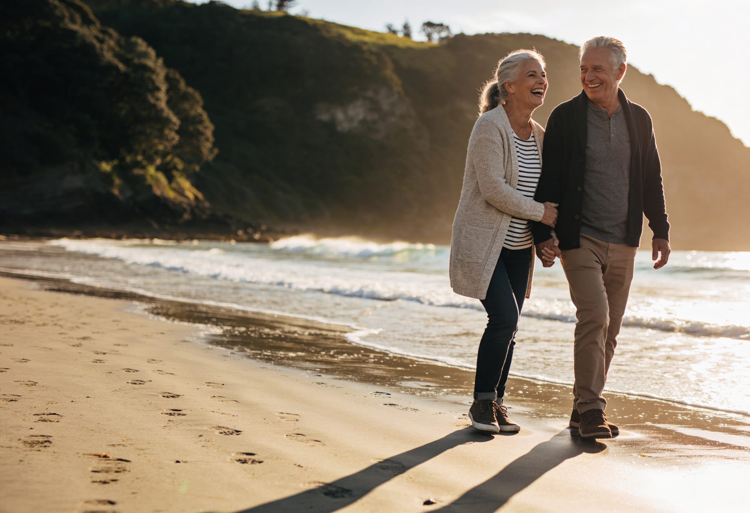 A happy older couple walking hand in hand on a Tauranga beach at golden hour